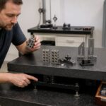 A metrology technician compares riser blocks and tooling on a granite surface plate while checking the adjustable stand underneath.